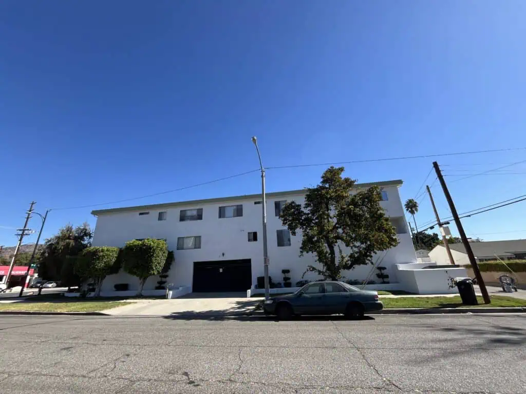 Modern white residential building with trees and parked cars under a clear blue sky.